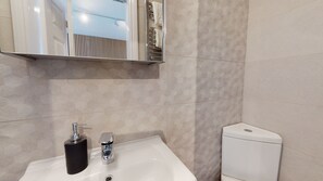 Baño con lavamanos blanco, dispensador de jabón negro, grifo cromado y inodoro blanco.