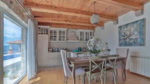 A dining area with a wooden table and chairs, a chandelier, and a view of the kitchen. - Villa Vista (Petrovac)