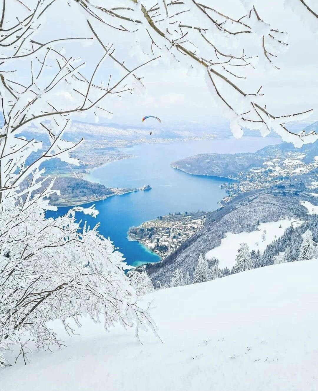 Vista panoràmica d'un paisatge cobert de neu, amb un llac i una vila a la distància.