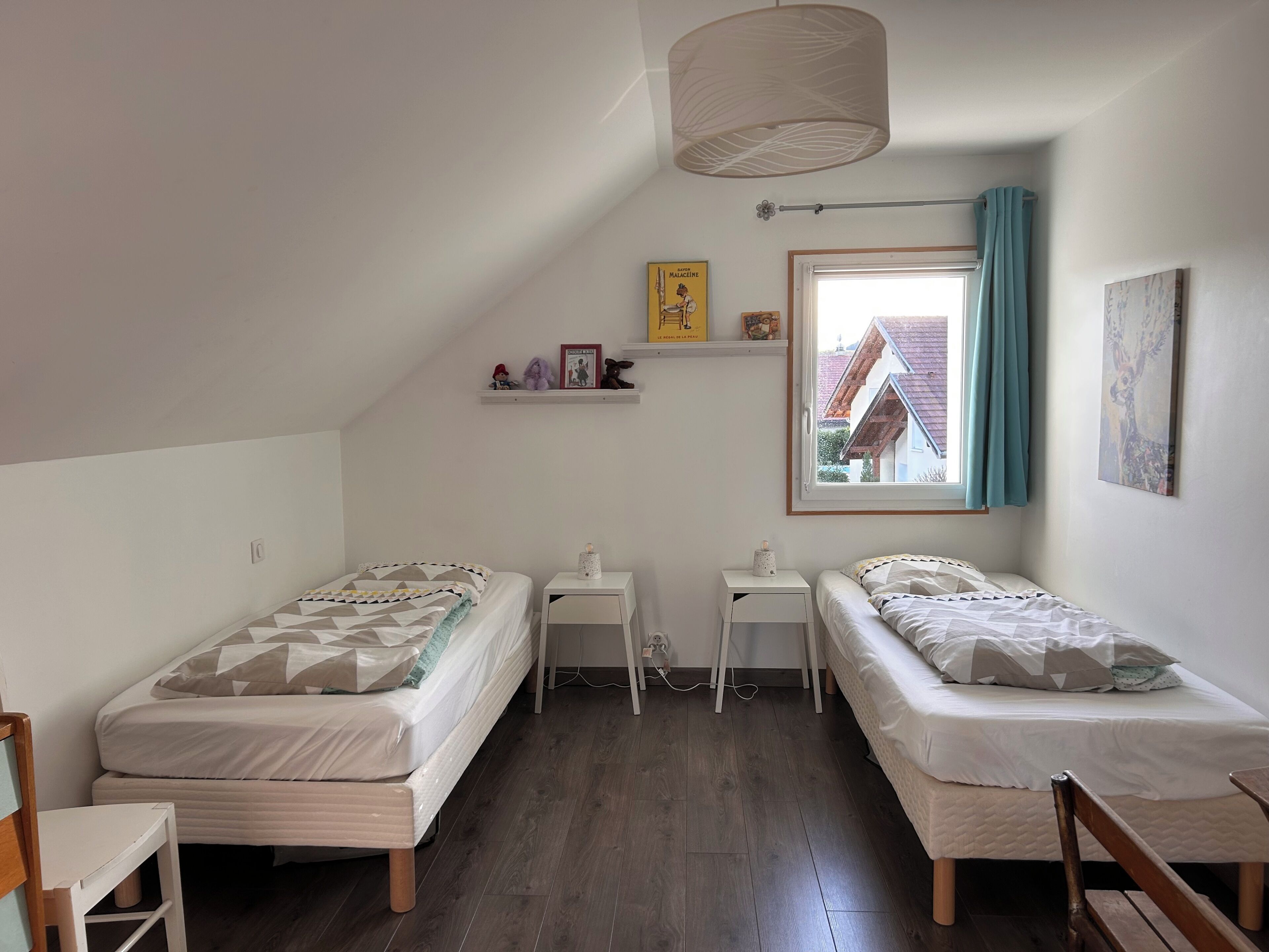 Un dormitorio con dos camas, una ventana con vistas, un estante con adornos y una lámpara de techo.