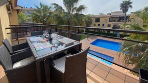 Ein Balkon mit Glastisch, Korbstühlen und einem Pool.