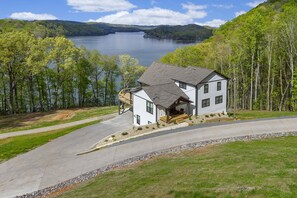 Une maison à deux étages avec un porche, entourée d’une allée et offrant une vue sur un lac.