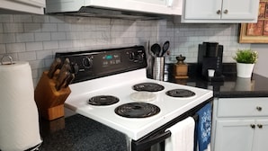 Una cocina con armarios blancos, una estufa de cuatro quemadores, un microondas y una cafetera.