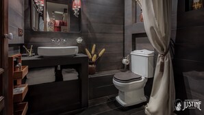 Un bagno moderno con piastrelle scure, un lavandino bianco, un water e uno specchio con illuminazione decorativa.