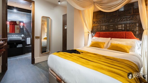 Camera d'albergo con un letto, uno specchio, un lavabo e una porta che dà su un'altra stanza.