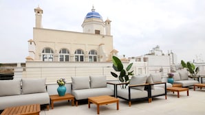 A rooftop terrace with a beige sofa set, wooden tables, and potted plants. - Goodnight Cádiz Apartments (Cádiz)