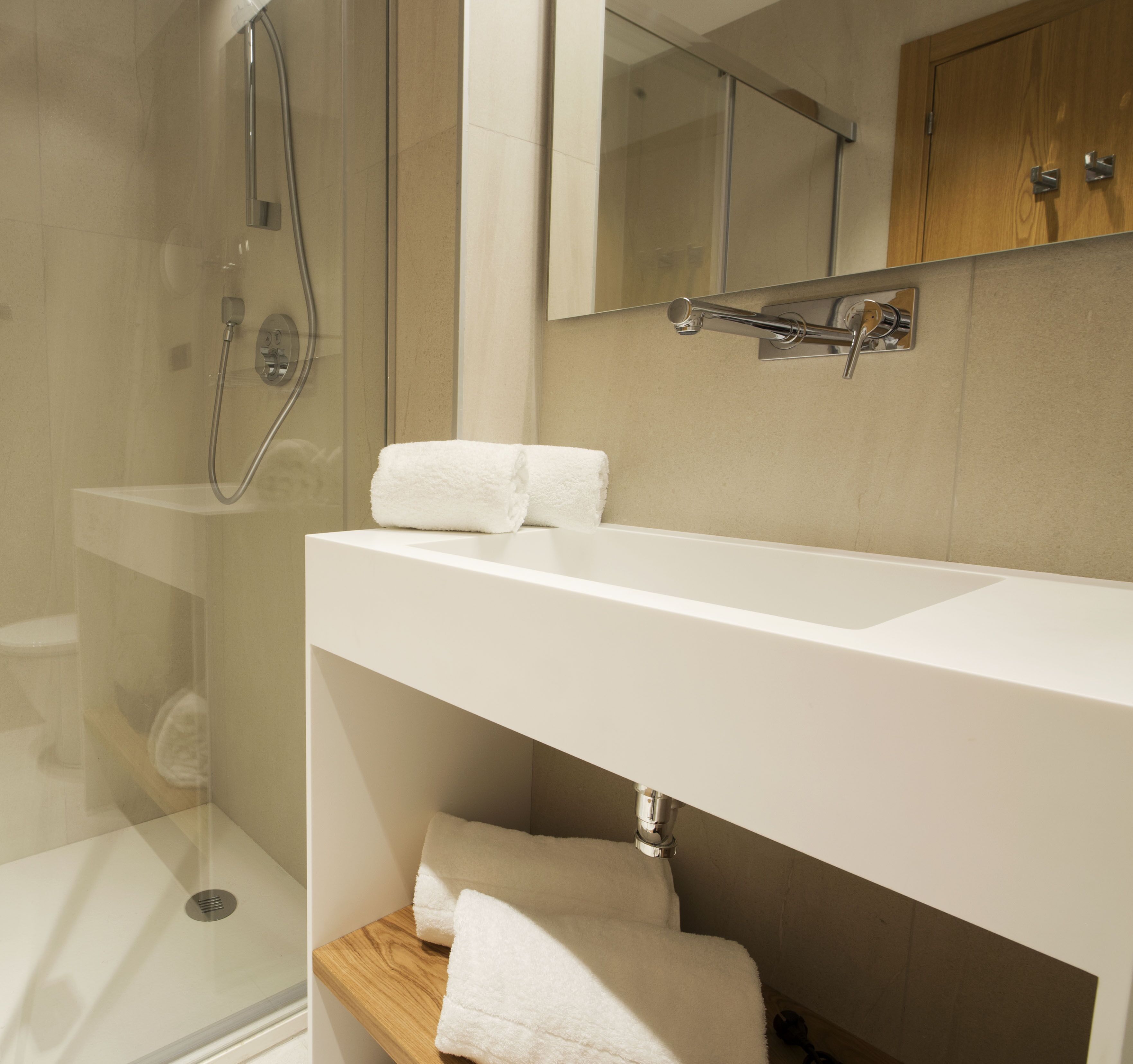 A modern bathroom with a glass-enclosed shower, a white sink, and a wooden shelf with towels.