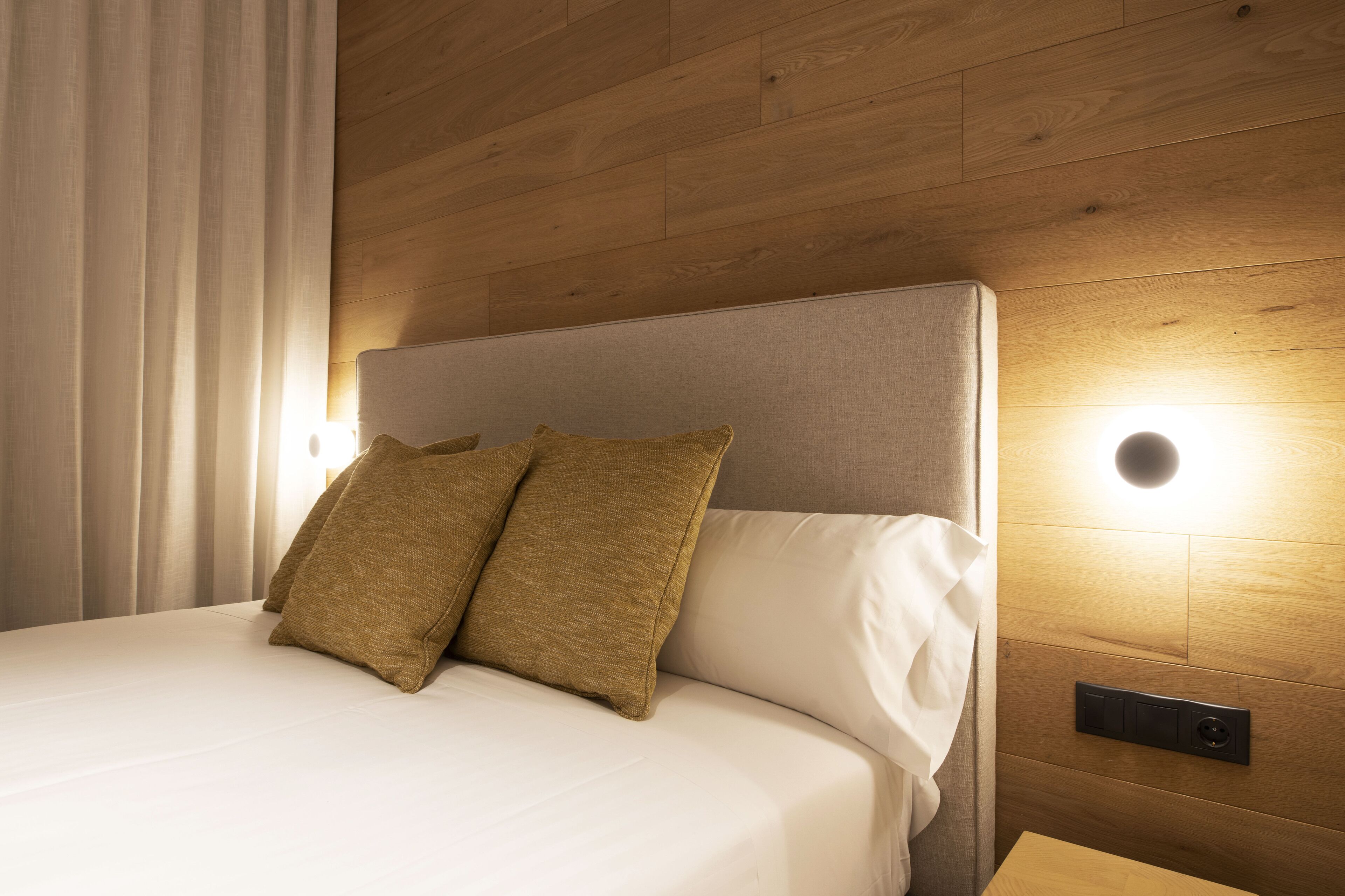 A neatly made bed with two pillows, a wooden headboard, and a wall-mounted light fixture.