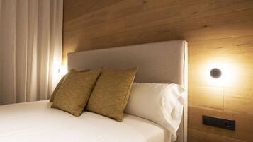 A neatly made bed with two pillows, a wooden headboard, and a wall-mounted light fixture.