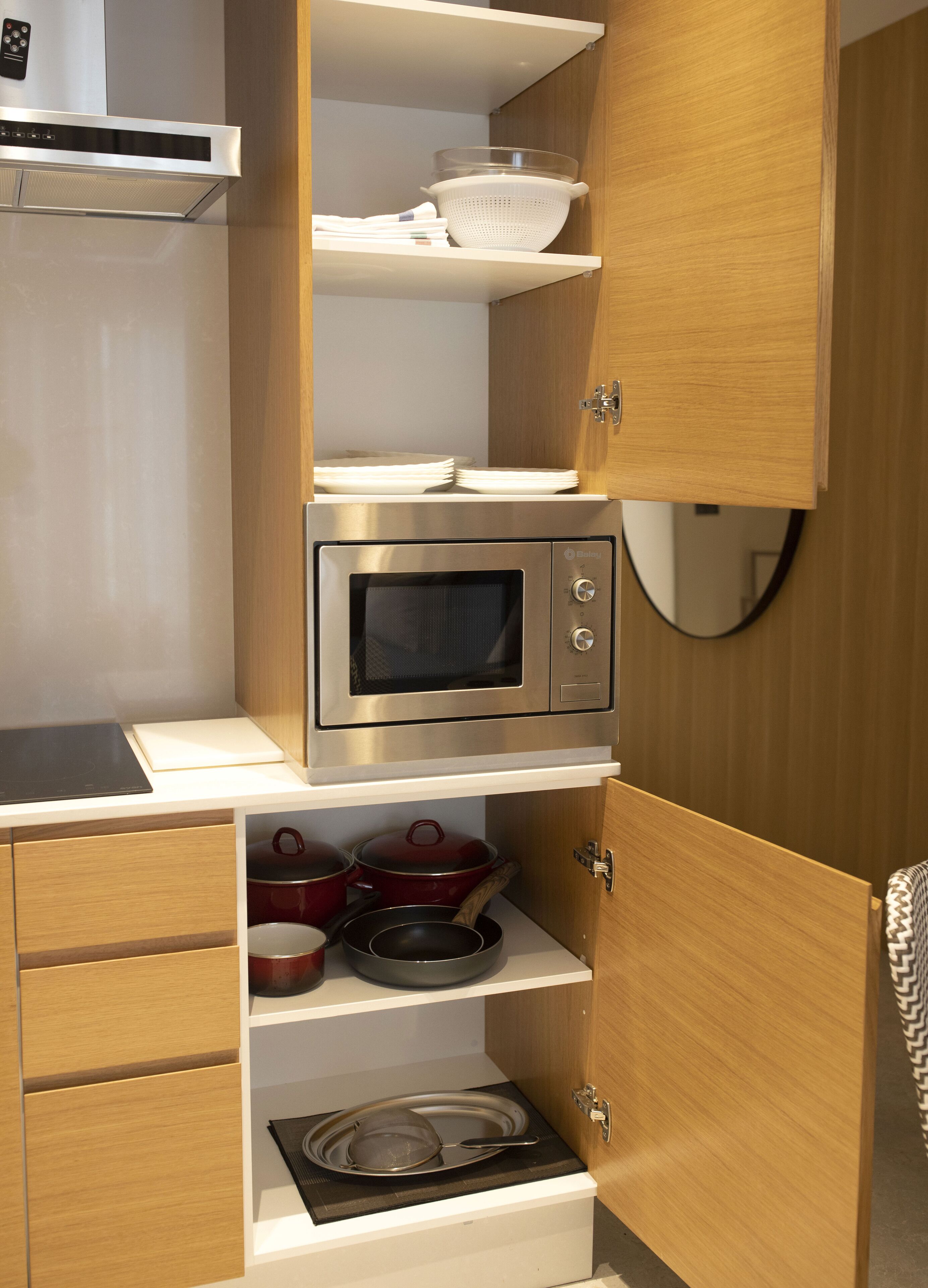 A compact kitchen with a built-in microwave, wooden cabinets, and a stainless steel range hood.