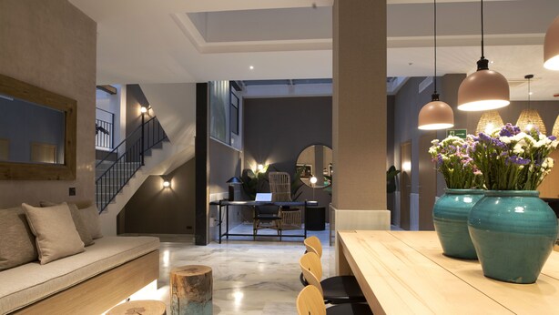 A modern interior with a sofa, wooden chairs, a dining table, and a staircase. - Goodnight Cádiz Apartments (Cádiz)