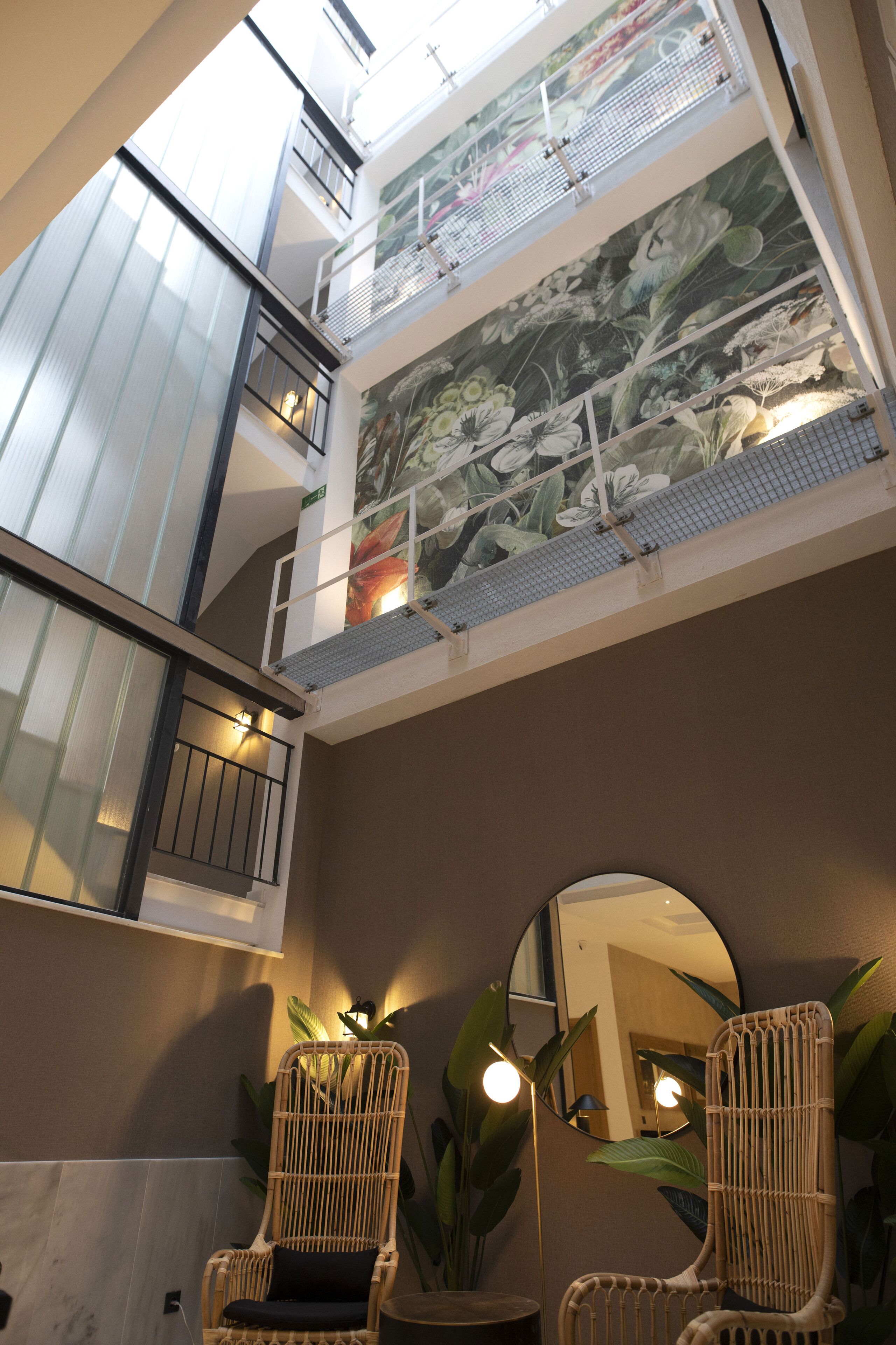 Ein mehrgeschossiges Interieur mit Balkon, einer großen Blumenwand, Korbsesseln und einem runden Spiegel.