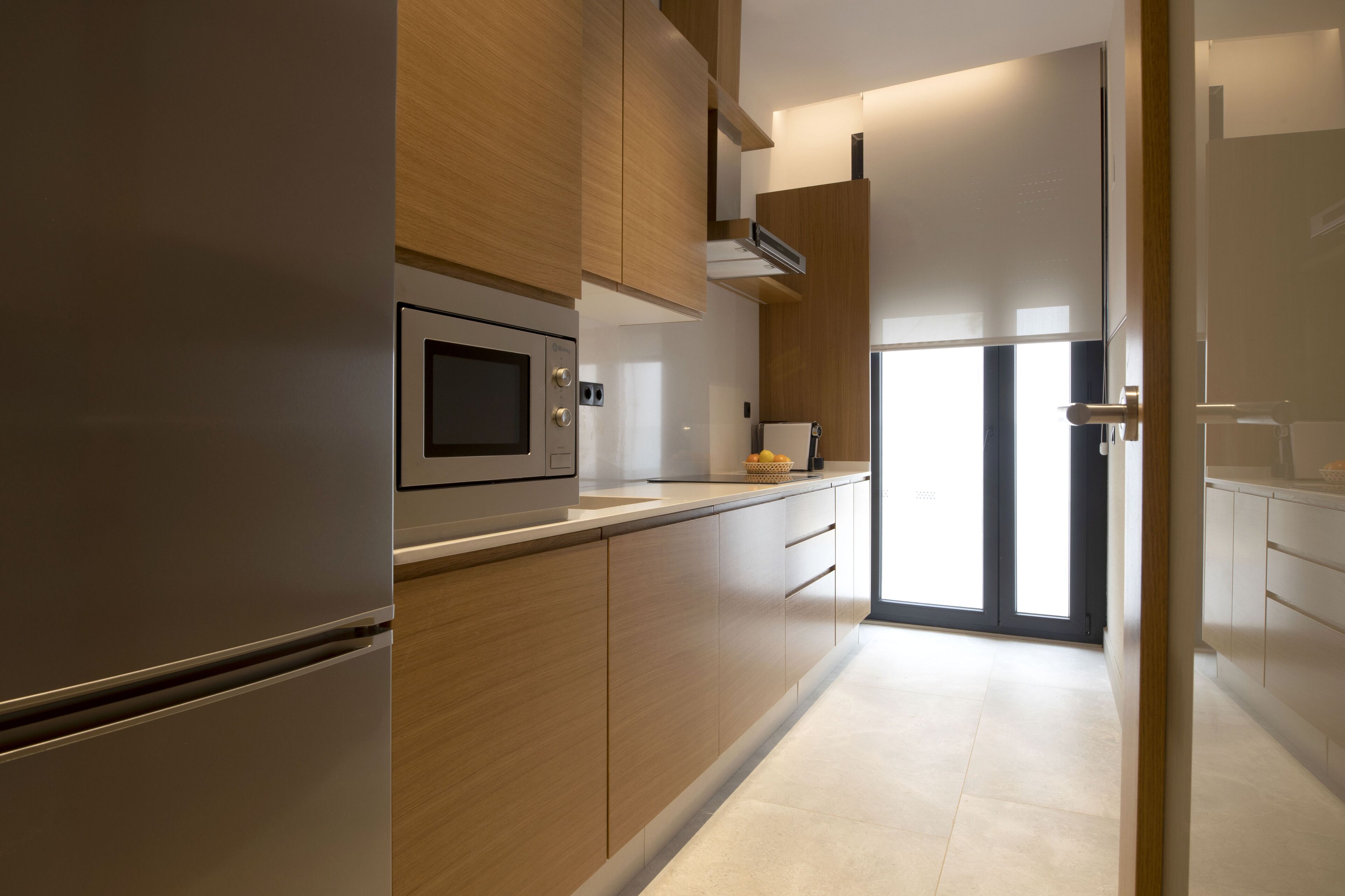A modern kitchen with wooden cabinets, a built-in microwave, and a stainless steel refrigerator.