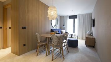 A modern hotel room with a dining area featuring wicker chairs, a round table, and a hanging light fixture.