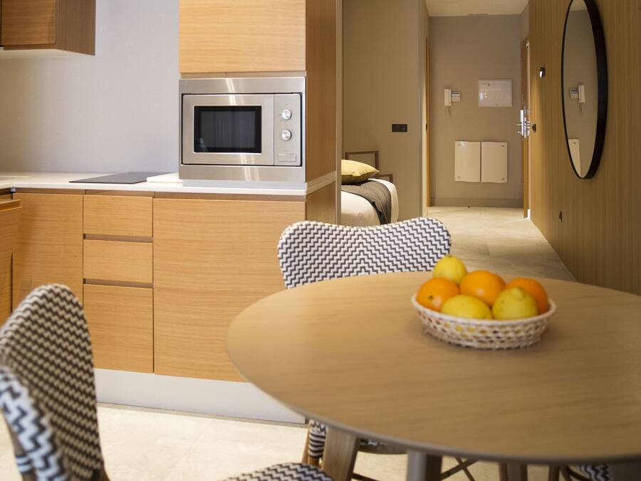 A modern kitchen with a built-in microwave, wooden cabinets, and a dining area with a round table and patterned chairs.