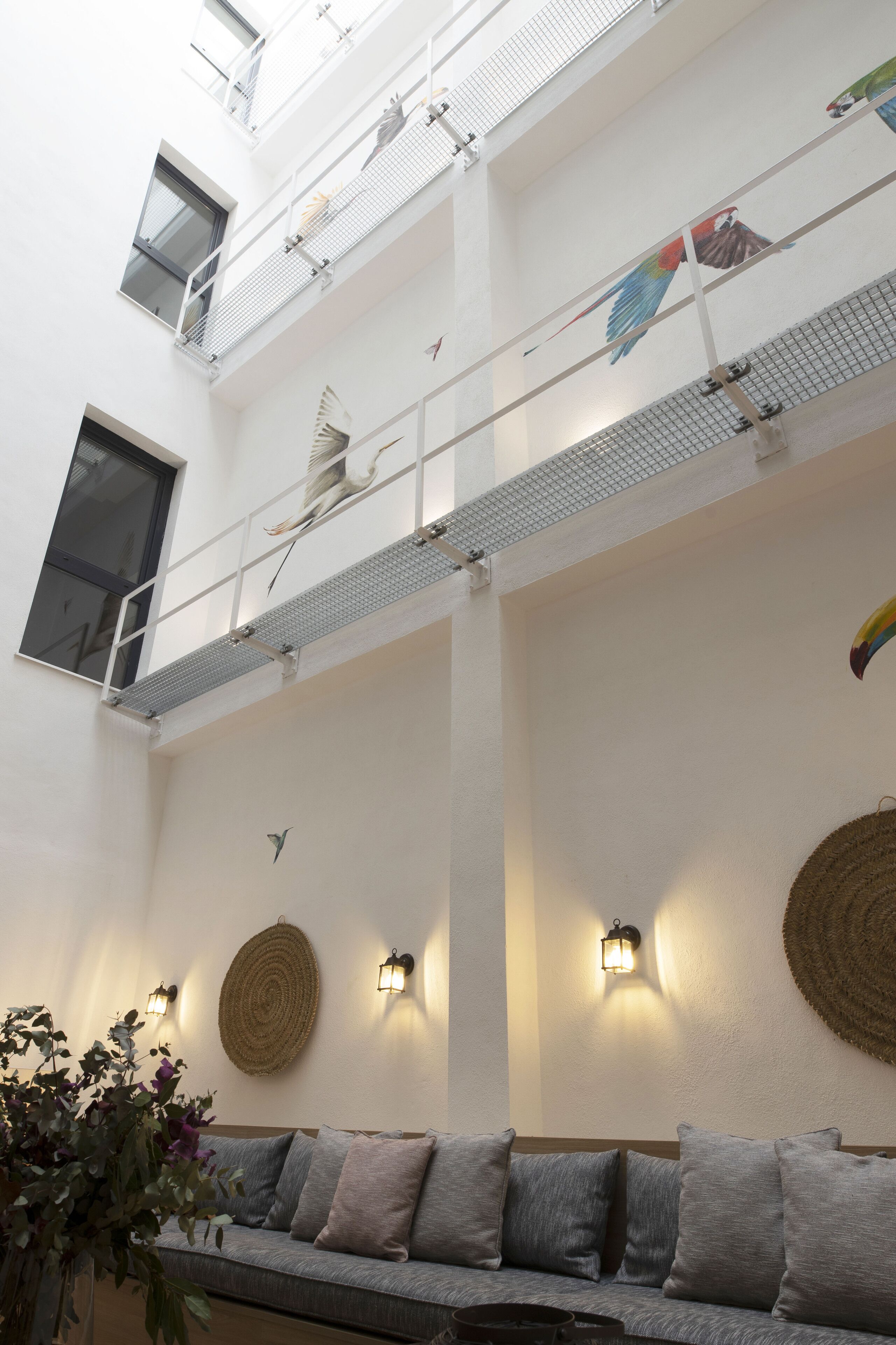 Een meerlaags interieur met een balkon, een bank, wandlampen en decoratieve wandversieringen.
