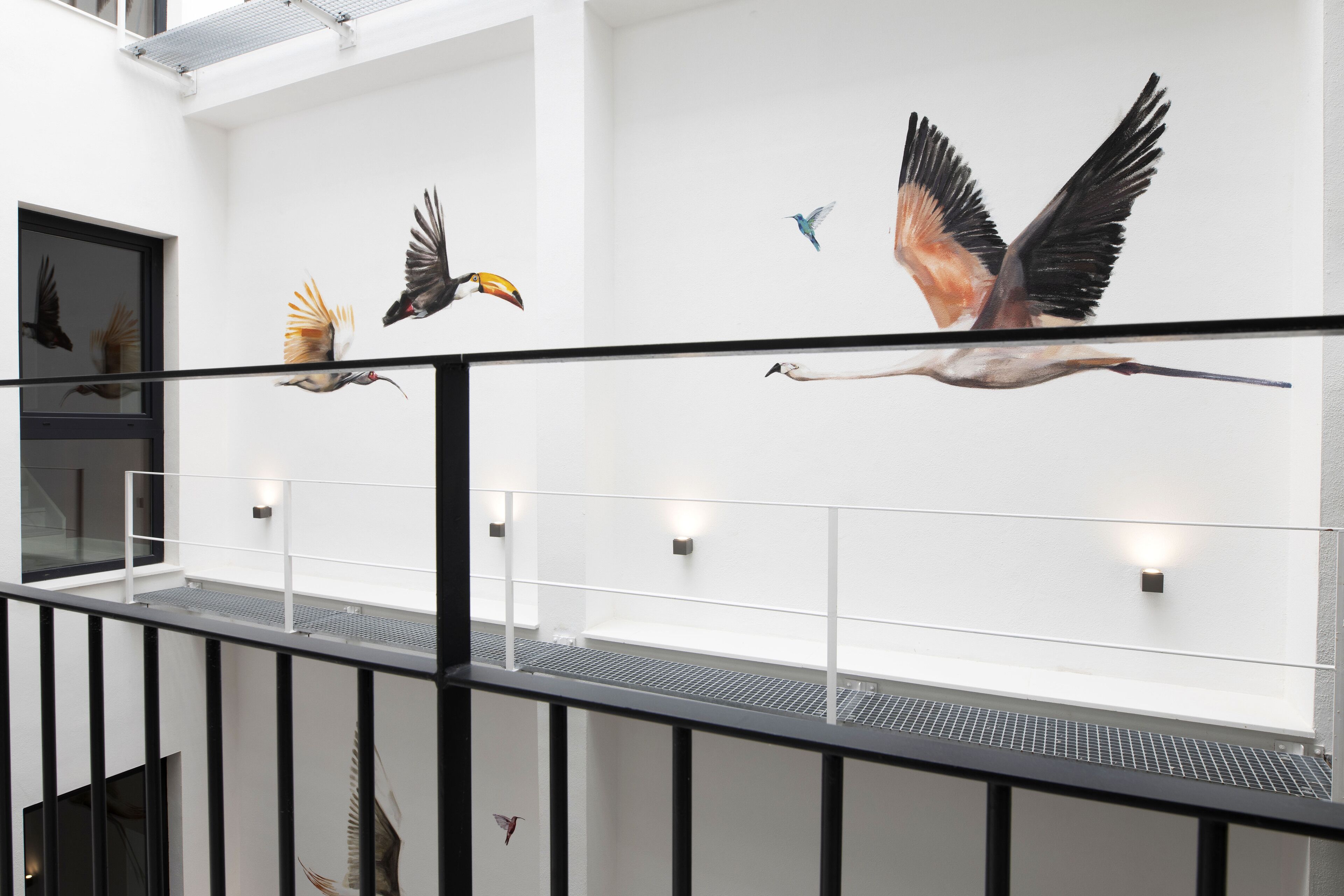 Un interior moderno con barandilla de vidrio que da a una pared decorada con murales de aves.