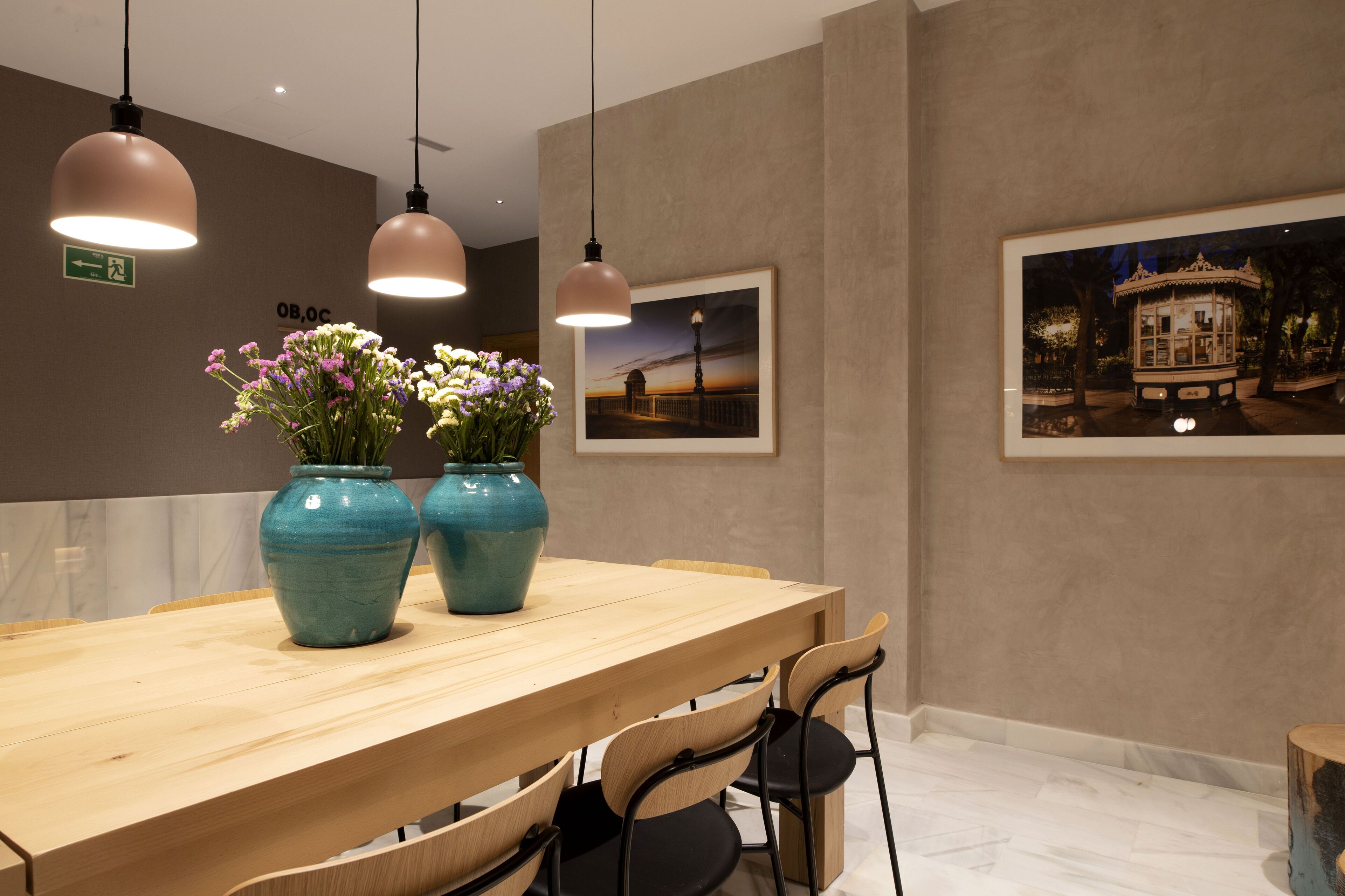 A wooden dining table with two vases of flowers, hanging pendant lights, and framed pictures on the wall.