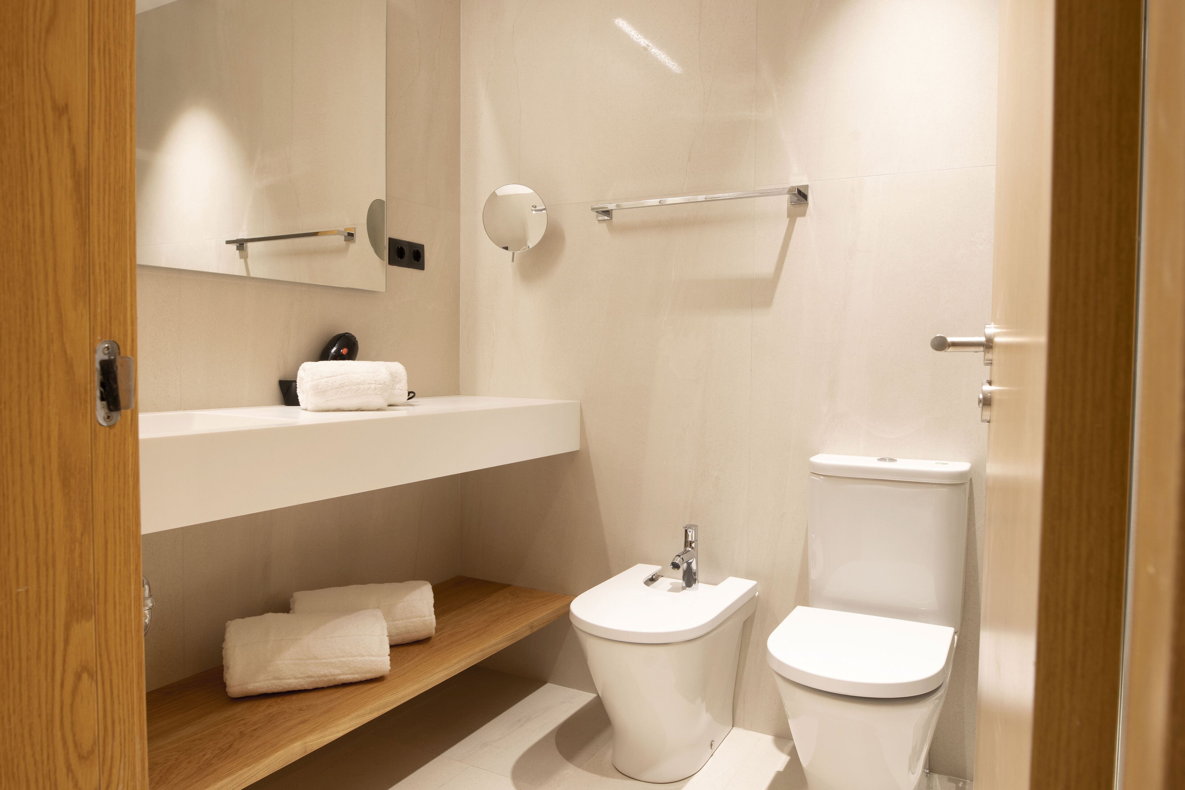 A modern bathroom with a toilet, bidet, and a wooden shelf with towels.