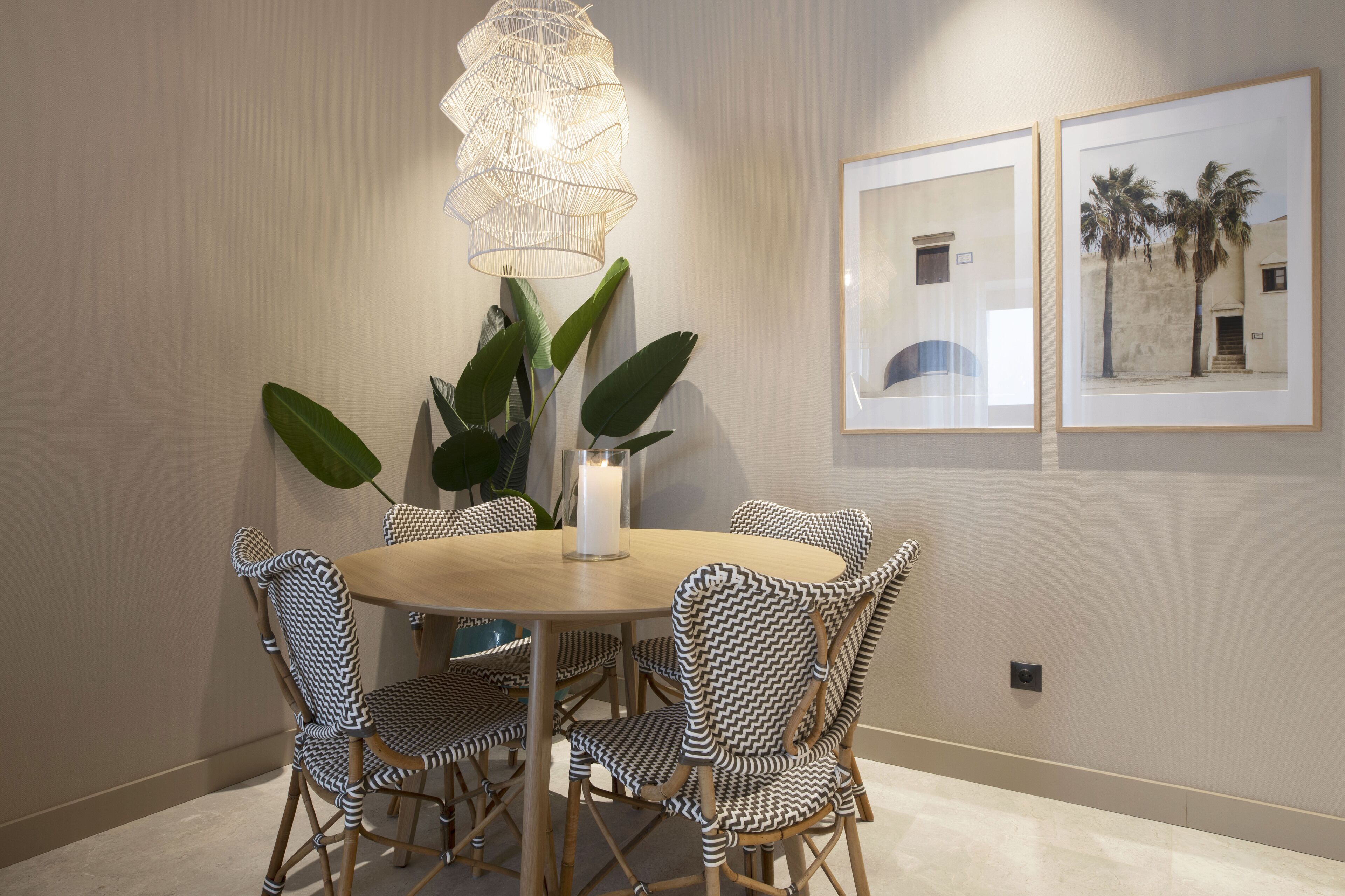 A dining area with a round table, black and white patterned chairs, a white candle centerpiece, a hanging light fixture, and two framed pictures on the wall.