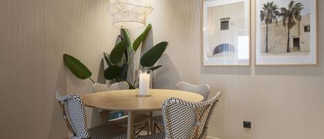 A dining area with a round table, black and white patterned chairs, a white candle centerpiece, a hanging light fixture, and two framed pictures on the wall.