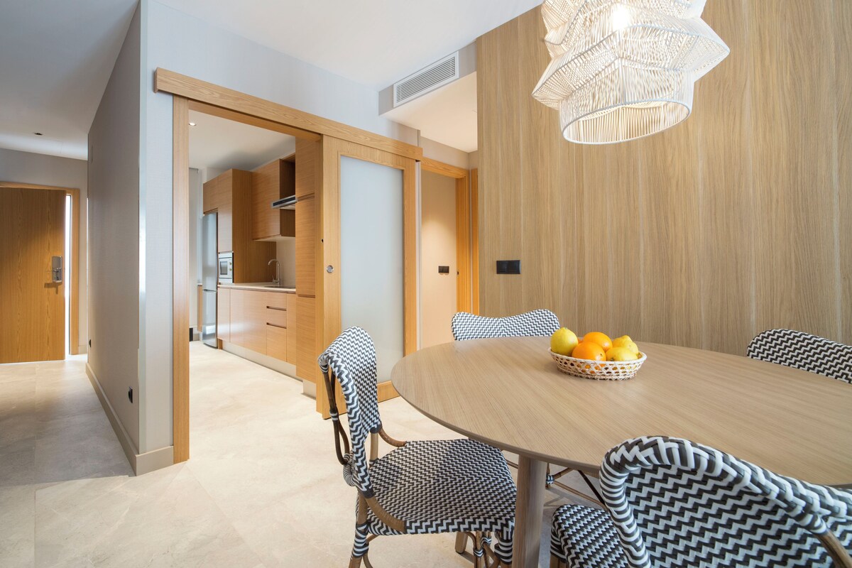 A modern dining area with a round table, patterned chairs, and a fruit basket.