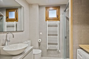 A modern bathroom with a large sink, a toilet, a glass shower enclosure, and a towel rack.