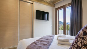 Quarto de hotel com uma cama grande, uma televisão de tela plana na parede e uma varanda com vista para as montanhas.
