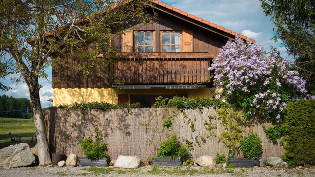 A wooden house with a balcony, surrounded by a wooden fence and various plants.
