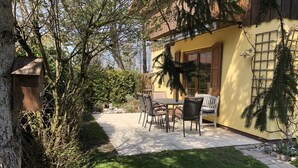 A patio area with a table and chairs, surrounded by a garden with trees and shrubs.