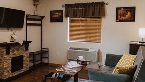 A cozy living room with a stone fireplace, a flat-screen TV, a grey sofa, and a ceiling fan.