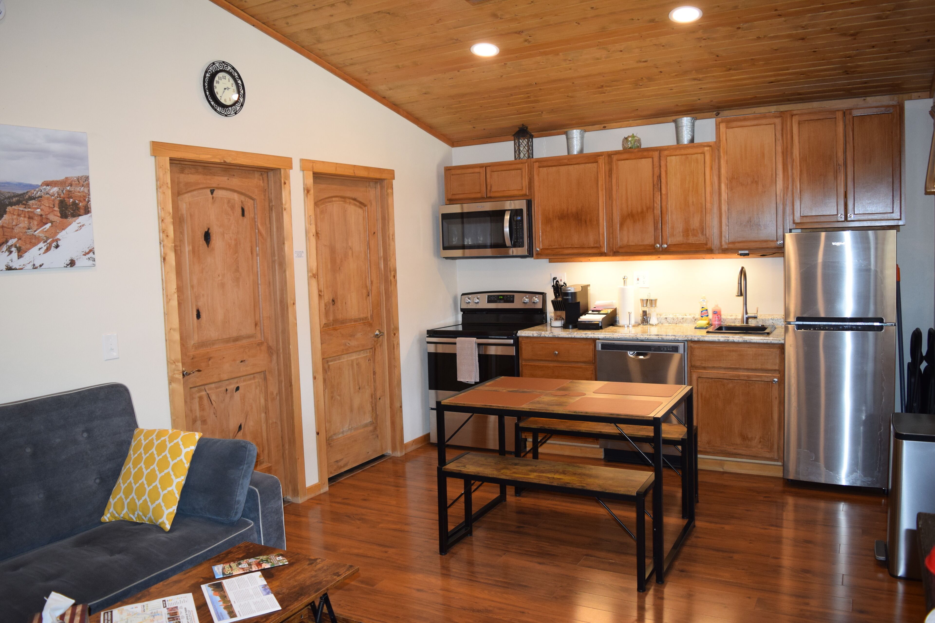 A compact kitchen with wooden cabinets, a stainless steel refrigerator, and a dining area with a table and benches.