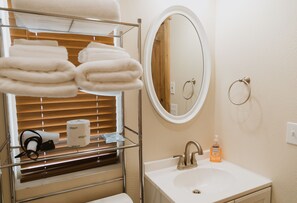 A bathroom with a sink, mirror, towel rack, and a window with blinds. - Quaint and spacious cabin in the heart of Bryce Canyon Country  (Cannonville)