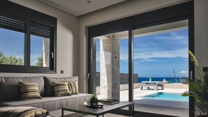 A modern living room with a sofa, coffee table, and a view of a pool and beach. - Sea Side LaLune Villa, with Heated Pool & Spa Whirlpool (Zakynthos)