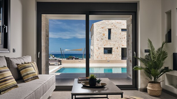 A modern living room with a large sliding glass door leading to a pool and a stone building. - Sea Side LaLune Villa, with Heated Pool & Spa Whirlpool (Zakynthos)