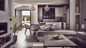 A modern living room with a sofa, coffee table, and chairs, a kitchen with a large window, and a dining area with a table and chairs. - Sea Side LaLune Villa, with Heated Pool & Spa Whirlpool (Zakynthos)