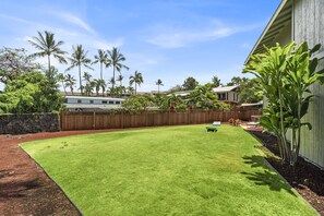 A backyard with a well-maintained lawn, a wooden fence, and palm trees.