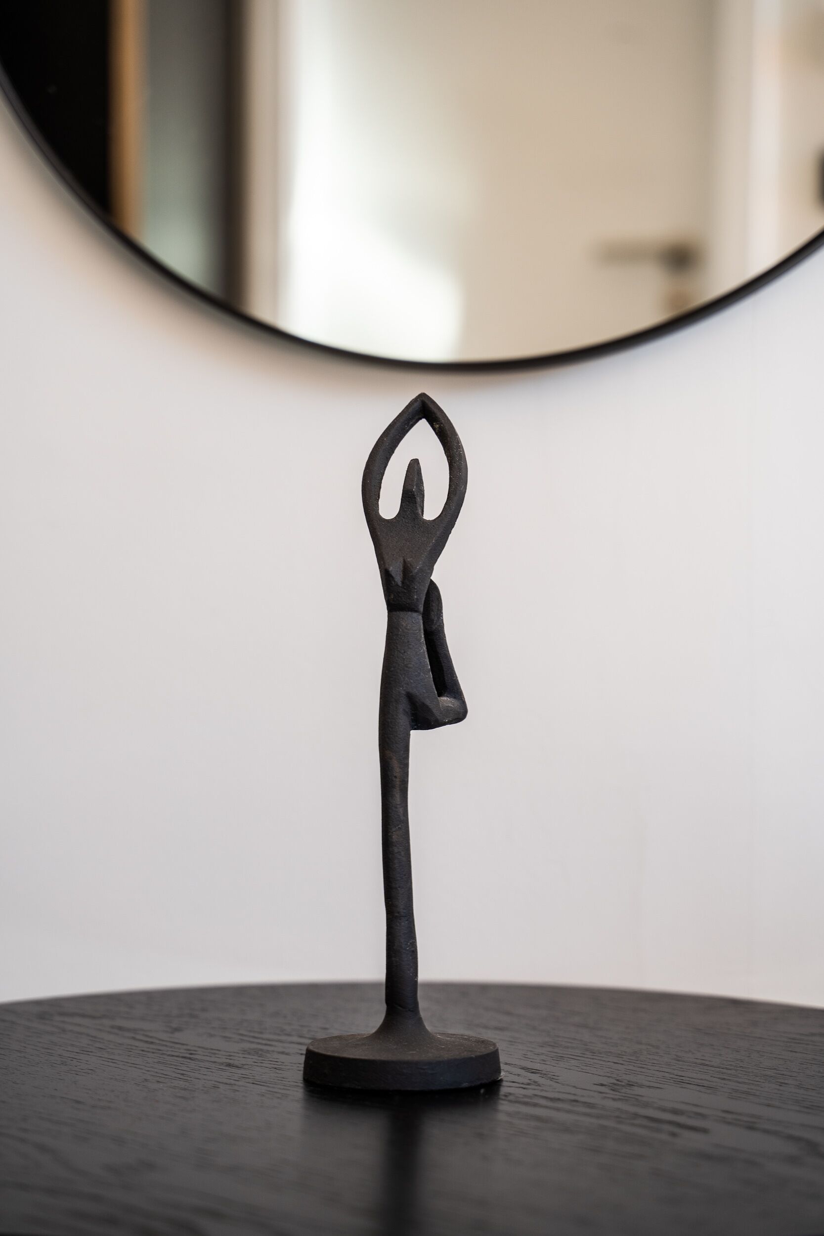 A black metal sculpture of a person in a yoga pose on a round table.