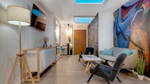 A modern living room with a sofa, coffee table, and a TV mounted on the wall. There is a skylight above the sofa and a colorful abstract painting on the wall. - Bed and Breakfast Sky (Zagreb)