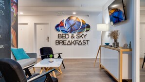 A modern breakfast area with a 'Bed & Sky Breakfast' sign, seating, a TV, and a minimalist decor. - Bed and Breakfast Sky (Zagreb)