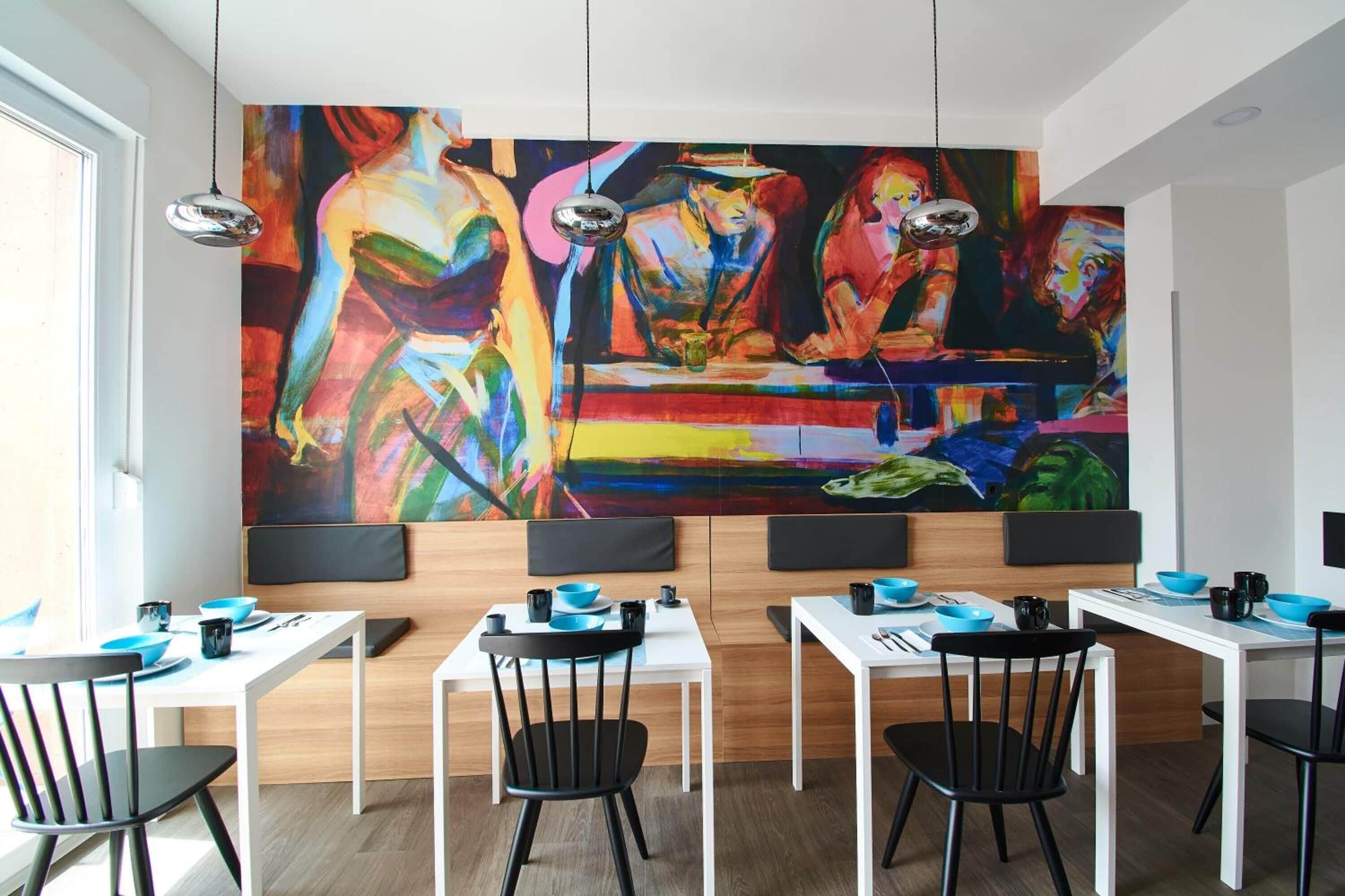 A modern dining area with white tables and black chairs, featuring vibrant abstract paintings on the wall.