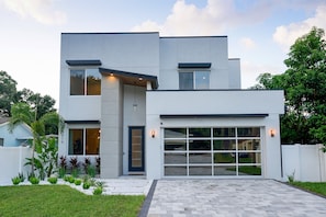 A modern two-story house with a garage, a well-maintained lawn, and a variety of plants.