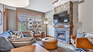 A living room with a stone fireplace, leather sofas, and a large window overlooking a residential area.