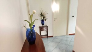 A hallway with a wooden bench, a blue vase with flowers, and a small table with a vase and flowers.