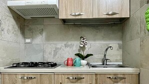 A kitchen with wooden cabinets, a gas stove, a sink, and a range hood. - Comodissimo Bilocale Dimora Raffaella (Torre Lapillo)
