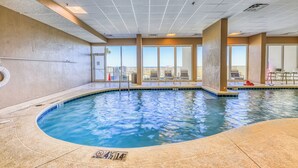 Una piscina interna con acqua cristallina, ampie finestre e vista sullo skyline della città.