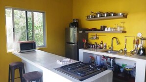 Een keuken met een gasfornuis, een koelkast en diverse keukengerei. Er is een raam met uitzicht op groen.