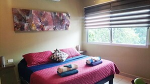 Een slaapkamer met een bed, kussens, een deken en een raam met zonwering.