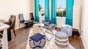 Un salón moderno con una mesa de centro de vidrio, cortinas color esmeralda y vistas a palmeras y edificios.