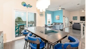 Una sala moderna con una mesa de comedor de vidrio, sillas azules, un sofá y una escalera.